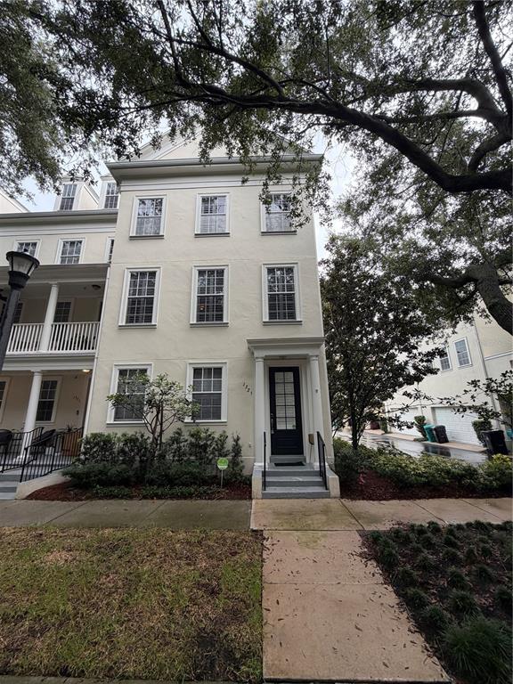 A three-story light-colored townhouse with a black front door and a sidewalk in front — 1325 COMMON WAY ROAD, ORLANDO, FL