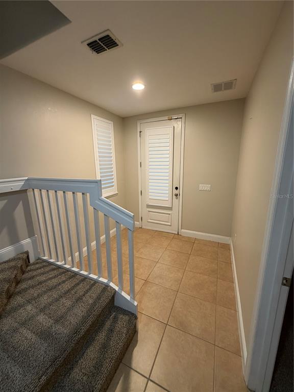 A landing with tan tile flooring, a white door, and a carpeted staircase with railings — 1325 COMMON WAY ROAD, ORLANDO, FL