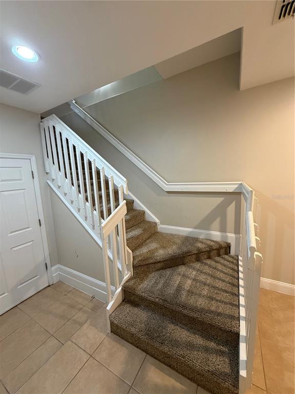 A carpeted staircase with white railings leads upward in a room with tiled flooring — 1325 COMMON WAY ROAD, ORLANDO, FL