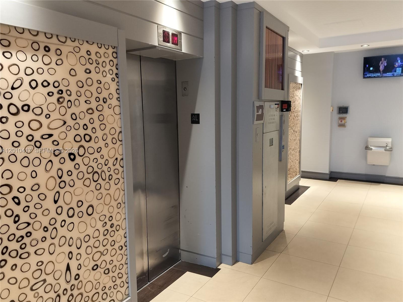 An elevator lobby features patterned wall panels, stainless steel doors, and light-colored tile flooring — 12550 Biscayne Blvd # 605, North Miami FL 33181, NORTH MIAMI, FL