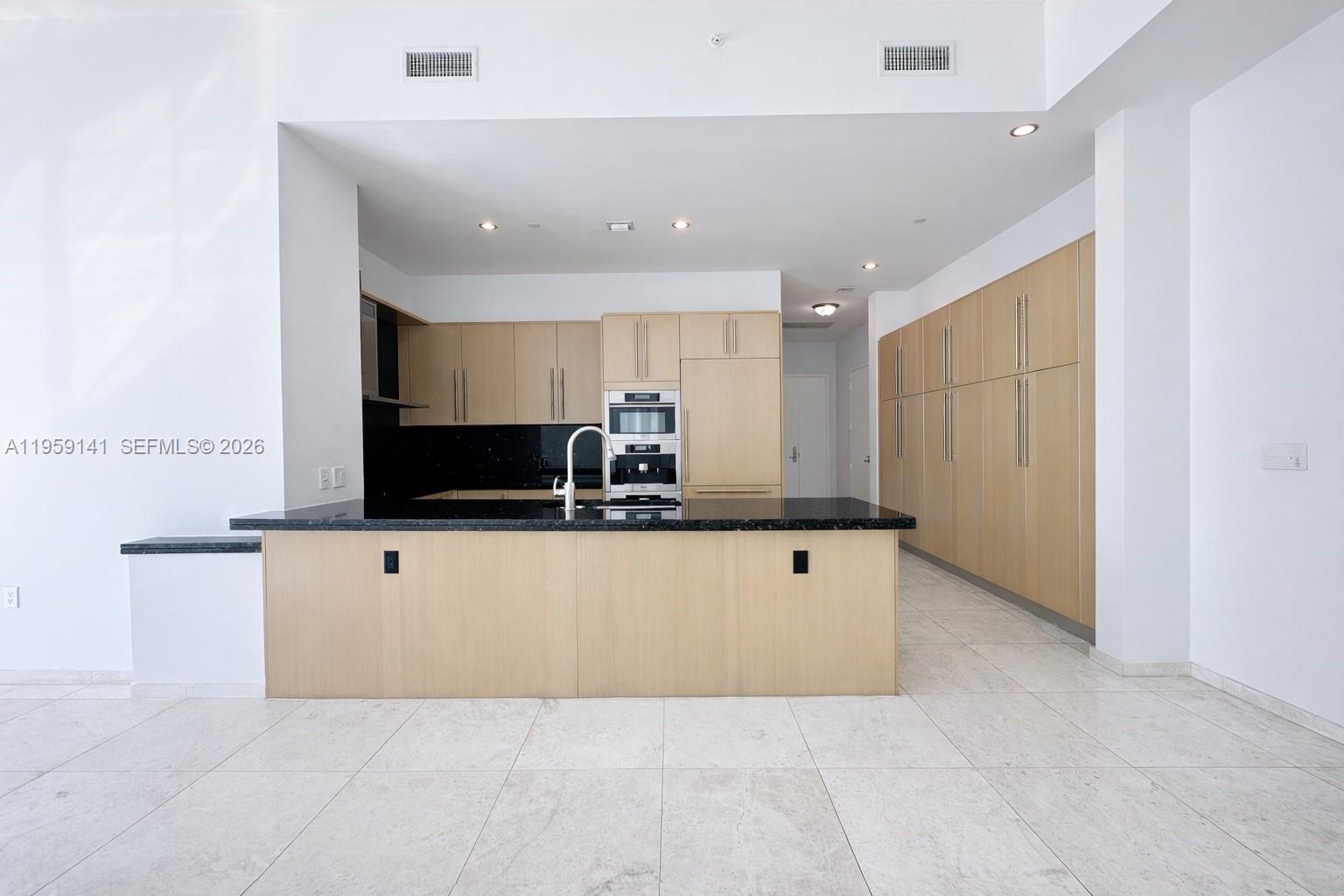 A modern kitchen features light wood cabinetry, a black granite island, and white tile flooring — 900 Brickell Key Blvd # 2405, Miami FL 33131, MIAMI, FL