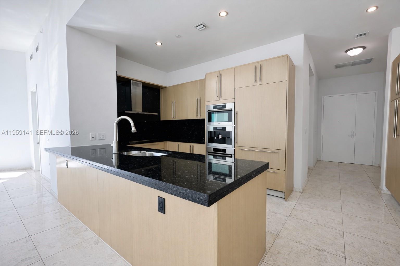 A modern kitchen features light wood cabinets, black granite countertops, and stainless steel appliances — 900 Brickell Key Blvd # 2405, Miami FL 33131, MIAMI, FL