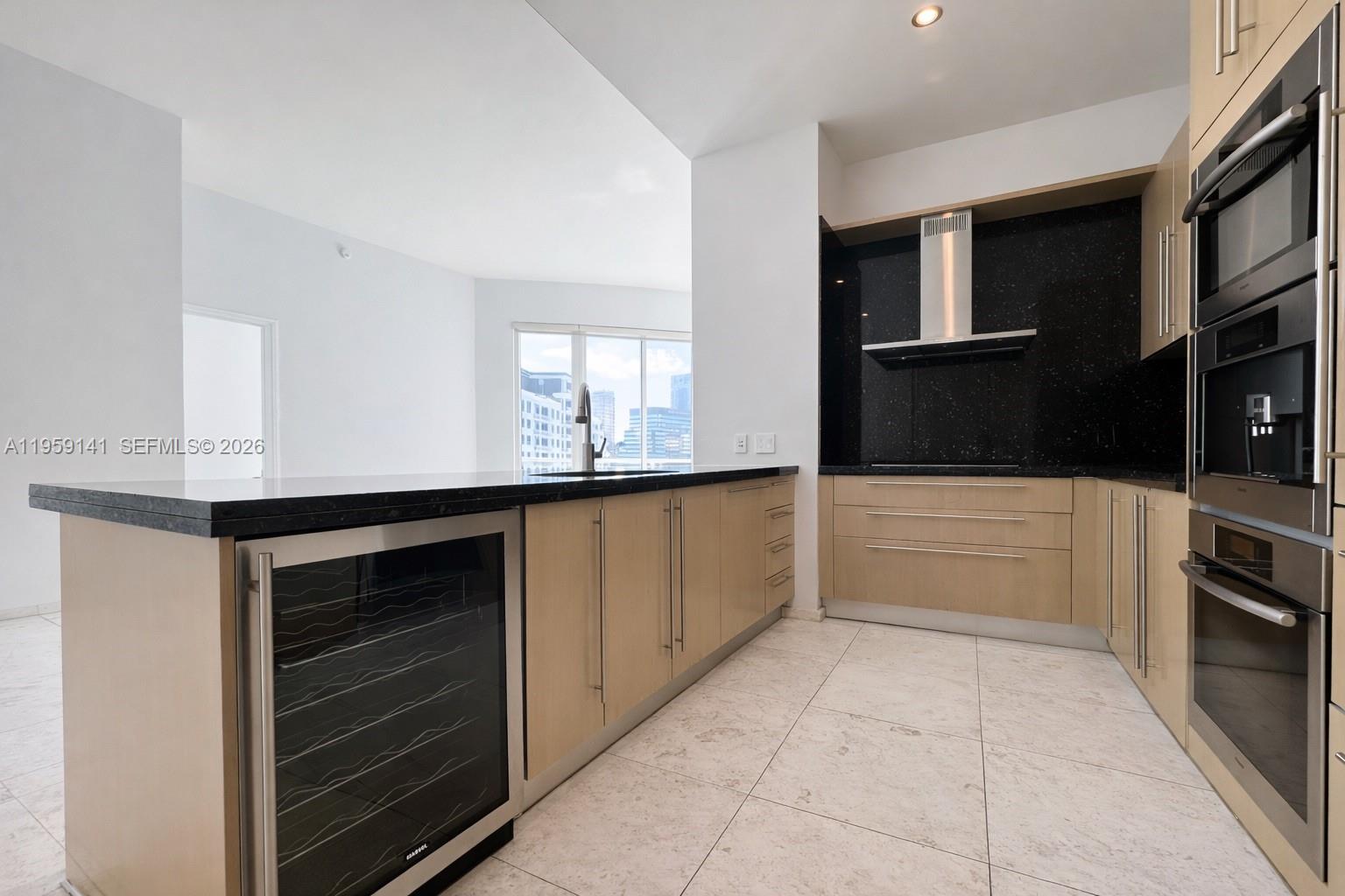 A modern kitchen features light wood cabinets, black countertops, a wine cooler, and stainless appliances — 900 Brickell Key Blvd # 2405, Miami FL 33131, MIAMI, FL
