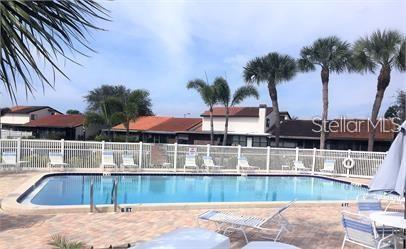 A rectangular swimming pool is surrounded by lounge chairs, a white fence, and palm trees — 7360 ULMERTON ROAD UNIT 4D, LARGO, FL