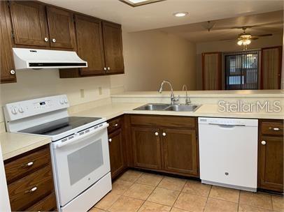 A kitchen features wood cabinets, white appliances, a double sink, and tile flooring — 7360 ULMERTON ROAD UNIT 4D, LARGO, FL