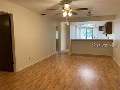 A living room with wood-look flooring and a ceiling fan opens to a kitchen area — 7360 ULMERTON ROAD UNIT 4D, LARGO, FL