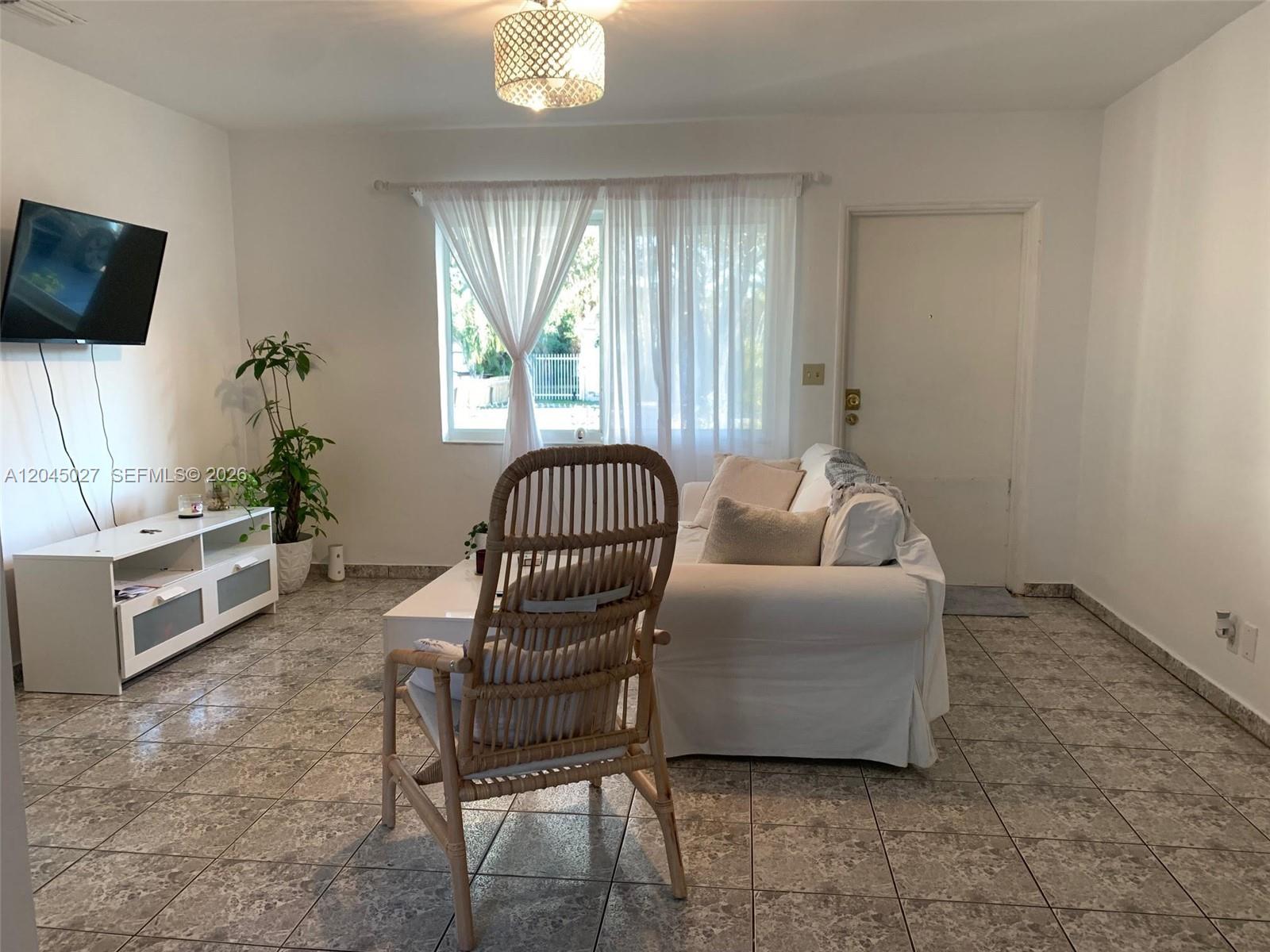 An empty room features white walls, a tiled floor, a window with curtains, and a chandelier — 2131 Arthur St # 0, Hollywood FL 33020, HOLLYWOOD, FL