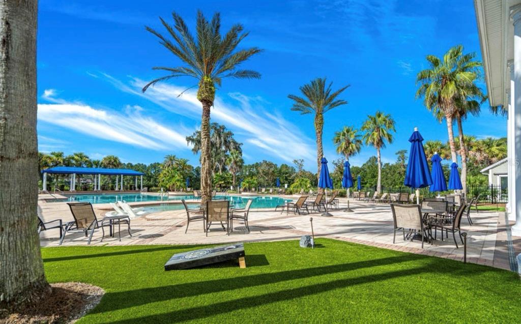 A swimming pool area features lounge chairs, tables with blue umbrellas, and a cornhole game — 19612 STERLING BLUFF WAY, BROOKSVILLE, FL