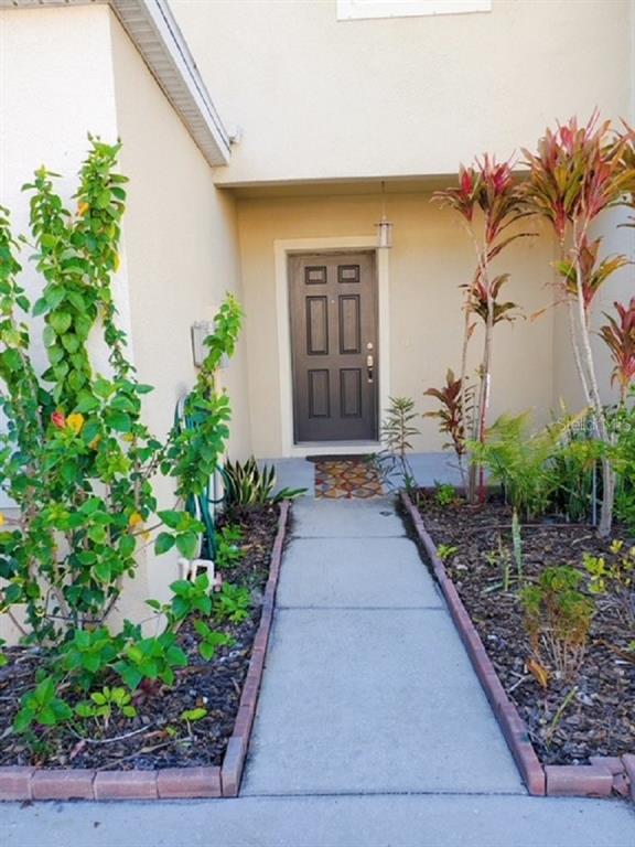 A concrete walkway leads to the dark front door of a home with landscaped gardens — 9907 HOUND CHASE DRIVE, GIBSONTON, FL