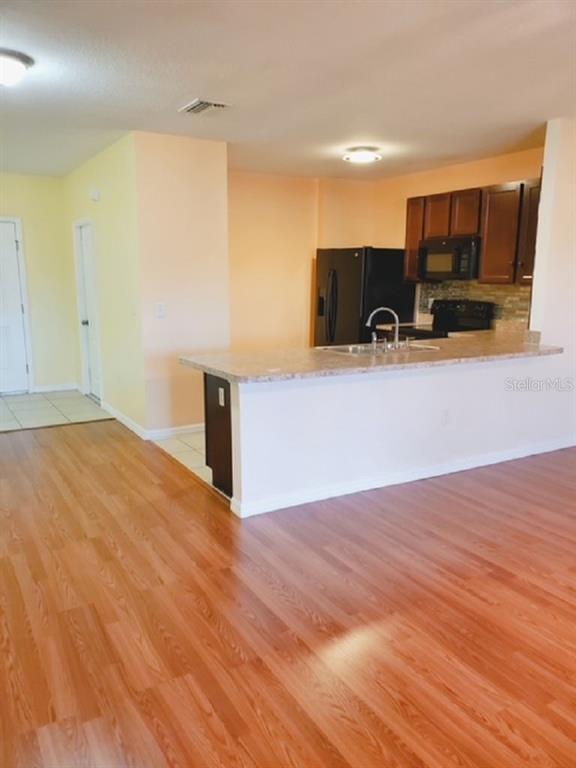 A kitchen with dark wood cabinets, black appliances, and a breakfast bar overlooks a room — 9907 HOUND CHASE DRIVE, GIBSONTON, FL