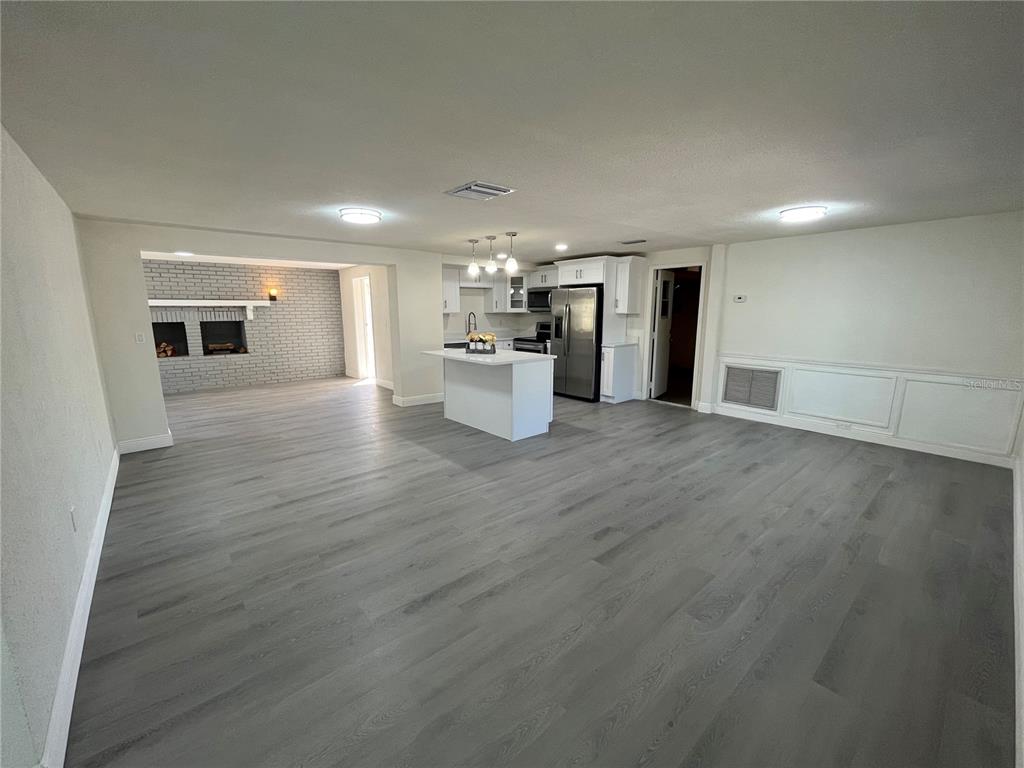 An open-concept living area features gray wood-look flooring, a white kitchen island, and a fireplace — 3314 COLUMBUS DRIVE, HOLIDAY, FL