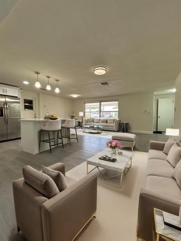 An open-concept living room and kitchen feature light wood flooring, neutral furniture, and pendant lighting — 3314 COLUMBUS DRIVE, HOLIDAY, FL