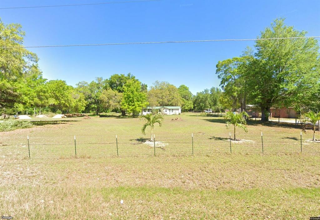 A wide, grassy lot features a wire fence, two small palm trees, and a distant house — 15425 TROUSDALE STREET, CLERMONT, FL