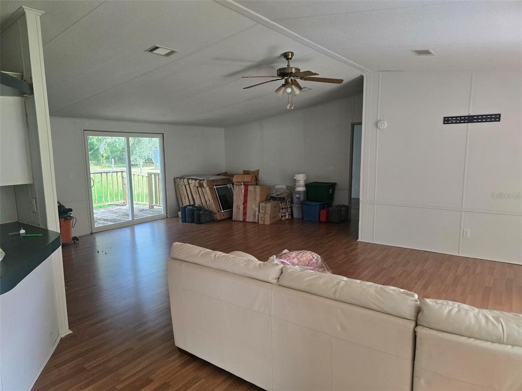 A living room with wood-look flooring, a ceiling fan, and a sliding glass door — 15425 TROUSDALE STREET, CLERMONT, FL