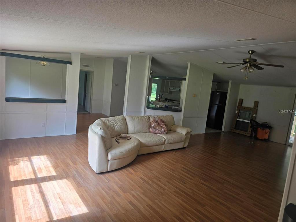 A living room with wood-look flooring, a beige sectional sofa, and an open kitchen — 15425 TROUSDALE STREET, CLERMONT, FL