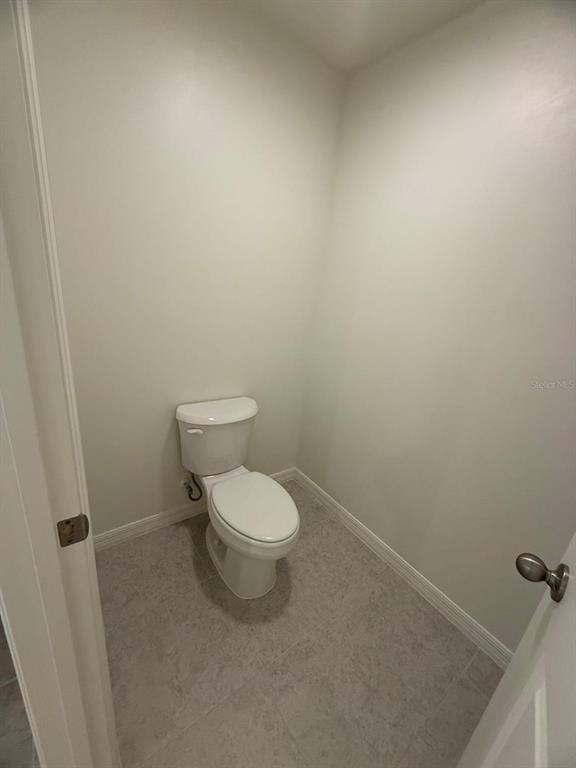 A small, windowless half bathroom featuring a white toilet and light gray tile flooring — 293 LAFLEUR STREET SW, PALM BAY, FL