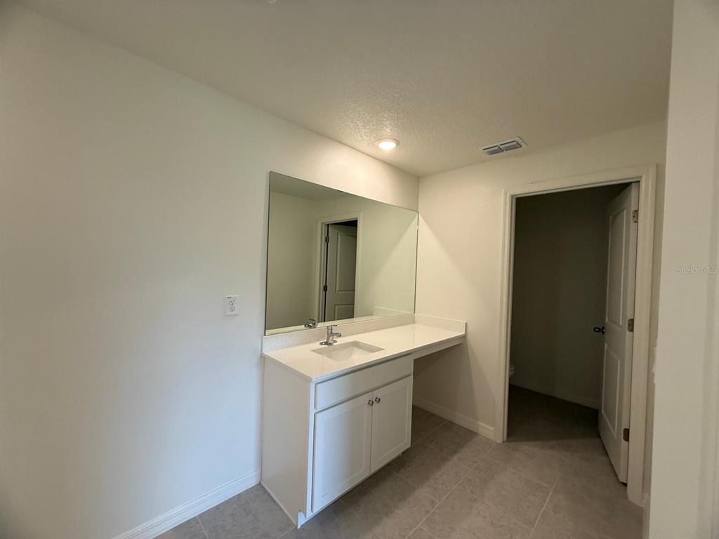 A bathroom vanity with a white countertop, single sink, and large mirror — 293 LAFLEUR STREET SW, PALM BAY, FL