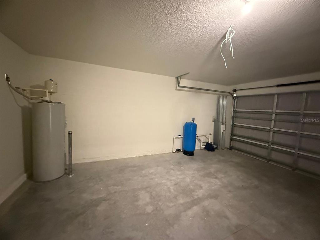 A garage interior features a water heater, a blue pressure tank, and a metal door — 293 LAFLEUR STREET SW, PALM BAY, FL