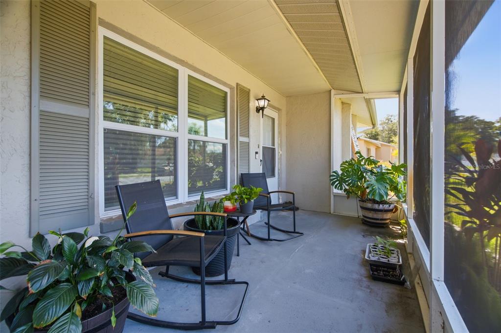 A screened-in porch features two rocking chairs, potted plants, and a light-colored exterior wall — 7907 DEER FOOT DRIVE, NEW PORT RICHEY, FL