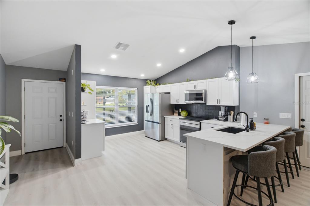 A modern kitchen features white cabinets, stainless steel appliances, a quartz island, and gray walls — 7907 DEER FOOT DRIVE, NEW PORT RICHEY, FL