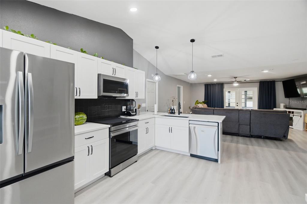 A kitchen with white cabinets, stainless steel appliances, and a black backsplash opens to a living area — 7907 DEER FOOT DRIVE, NEW PORT RICHEY, FL