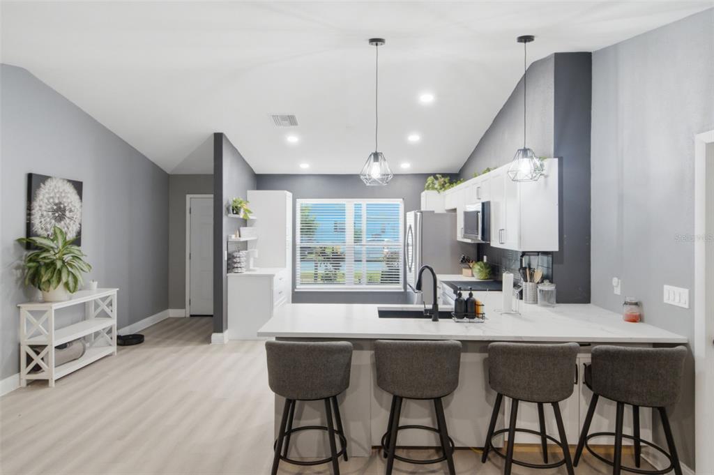 A modern kitchen features a white island with four gray stools and dark gray walls — 7907 DEER FOOT DRIVE, NEW PORT RICHEY, FL