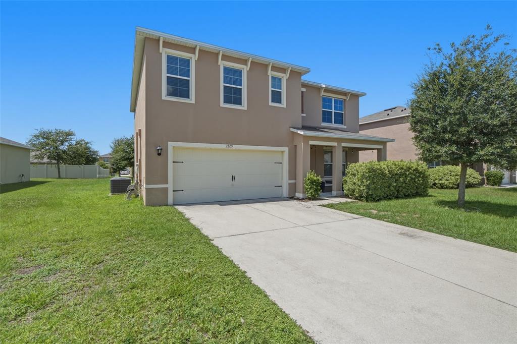A two-story suburban house with a beige stucco exterior, a two-car garage, and a driveway — 2609 GRAND CENTRAL AVENUE, TAVARES, FL