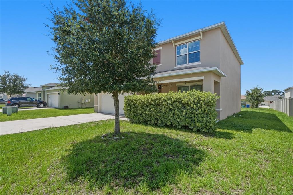 A two-story suburban house with a tan stucco exterior, a driveway, and a large hedge — 2609 GRAND CENTRAL AVENUE, TAVARES, FL