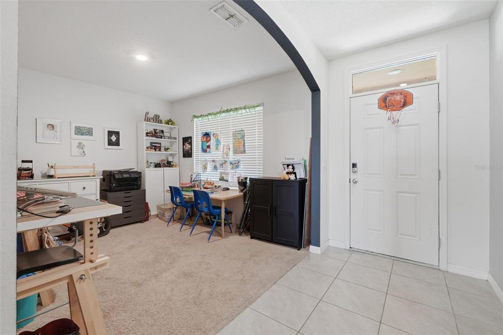 A room with carpeted flooring and a desk area sits beside a tiled entryway — 2609 GRAND CENTRAL AVENUE, TAVARES, FL