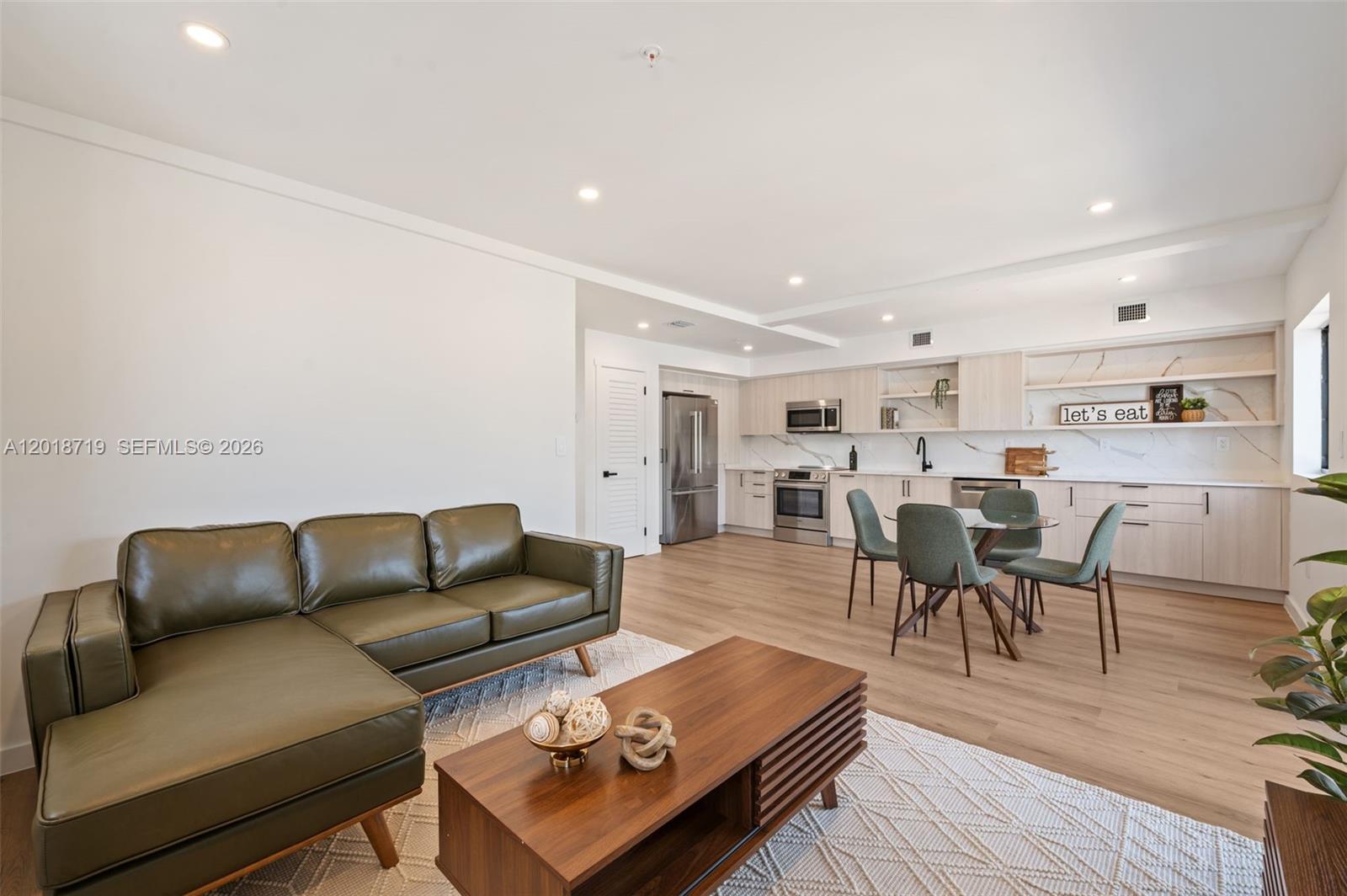 An open-concept living room and kitchen featuring a green sectional sofa and light wood cabinetry — 722 NW 55th Ter # 722, Miami FL 33127, MIAMI, FL