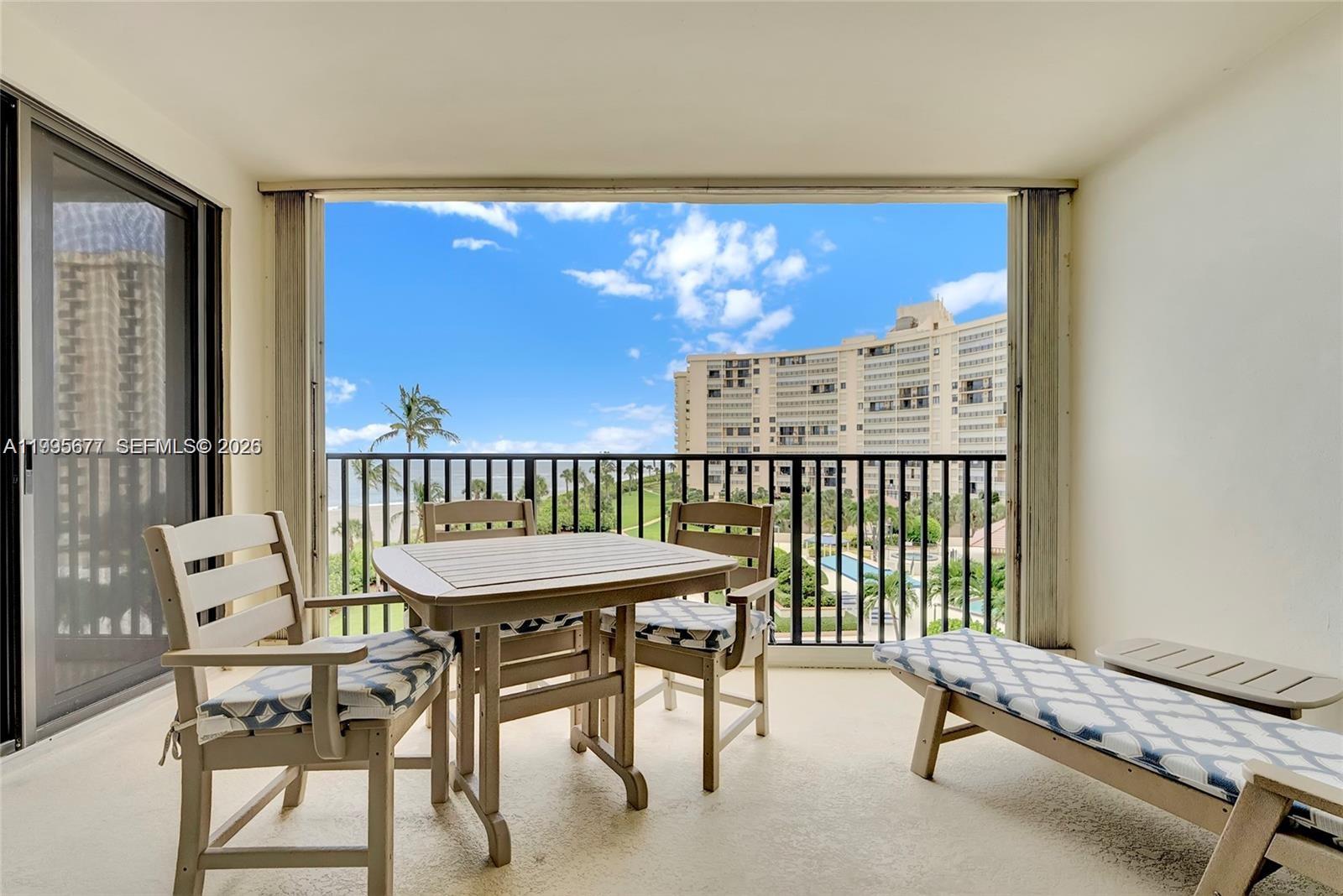 A balcony features a dining set and lounge chair overlooking a building and ocean view — 400 Ocean Trail Way # 401, Jupiter FL 33477, JUPITER, FL