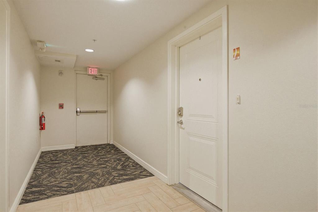 A hallway features a white door, an exit door with a crash bar, and flooring — 223 ISLAND WAY UNIT 2D, CLEARWATER BEACH, FL