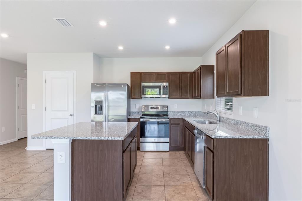 A kitchen features dark wood cabinets, granite countertops, stainless steel appliances, and tile flooring — 17131 11TH TERRACE E, BRADENTON, FL