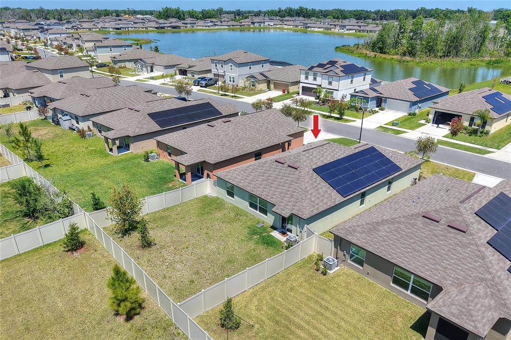 An aerial view shows suburban houses with solar panels and fenced backyards near a lake — 3603 NATURAL TRACE, PLANT CITY, FL