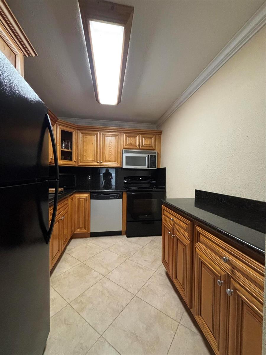A kitchen features wood cabinets, black countertops, stainless steel appliances, and light-colored tile flooring — 10084 S 42nd Dr Drive # 122, Boynton Beach FL 33436, BOYNTON BEACH, FL