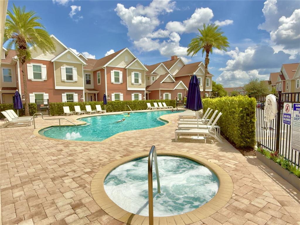 A swimming pool and hot tub are situated in front of multi-story residential buildings — 7498 SUNVILLE AVENUE, KISSIMMEE, FL