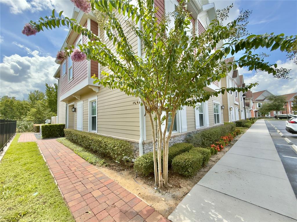 A multi-story building exterior with tan siding, a brick walkway, and a blooming crape myrtle — 7498 SUNVILLE AVENUE, KISSIMMEE, FL