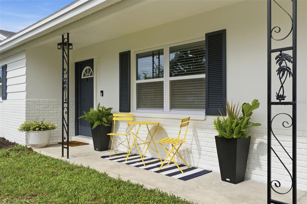 A white brick house exterior features a front porch with yellow bistro furniture and plants — 2048 JEFFERSON AVENUE, DUNEDIN, FL