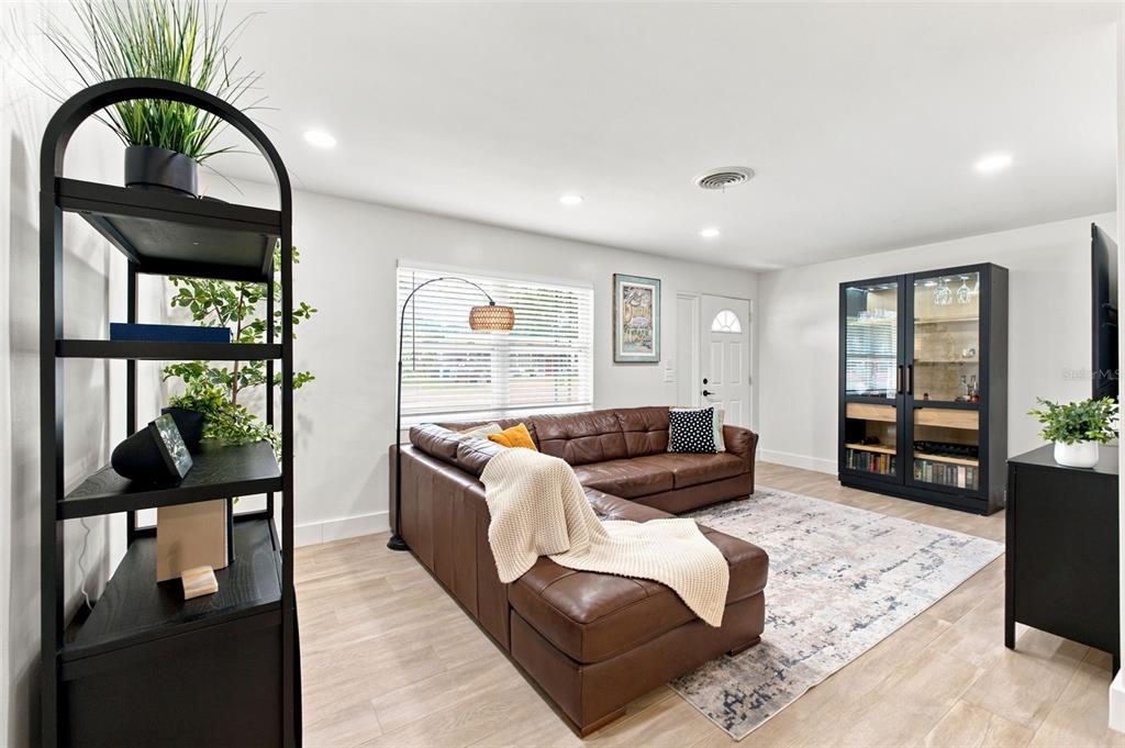 A living room features a brown leather sectional, a black display cabinet, and light flooring — 2048 JEFFERSON AVENUE, DUNEDIN, FL
