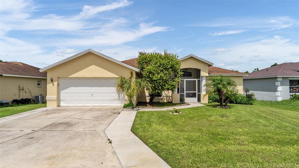 A single-story suburban house with a two-car garage, beige stucco exterior, and a front lawn — 3549 MANOR LOOP, LAKELAND, FL