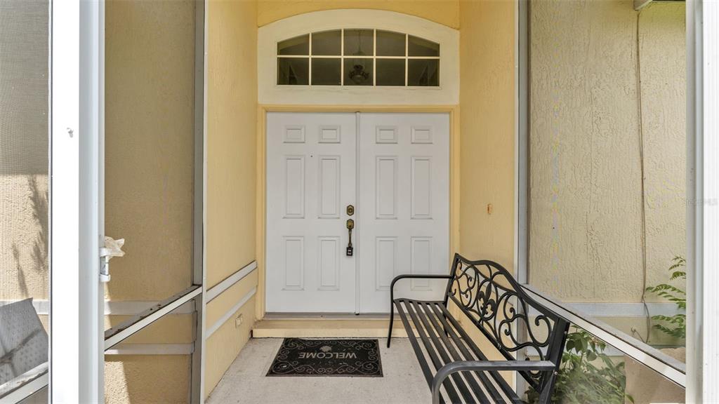 A covered entryway features a double white front door, a black metal bench, and a mat — 3549 MANOR LOOP, LAKELAND, FL