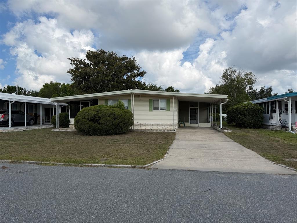 A single-story manufactured home with a concrete driveway, carport, and a large front yard bush — 12326 CONDE DRIVE, BROOKSVILLE, FL