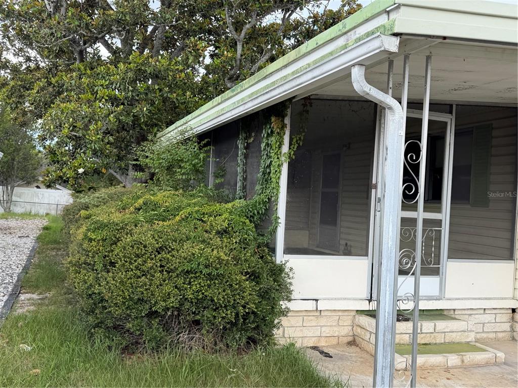 A mobile home exterior features a screened porch, overgrown landscaping, and a metal support column — 12326 CONDE DRIVE, BROOKSVILLE, FL