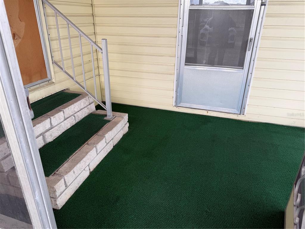 A covered porch features green outdoor carpeting, brick steps with a metal railing, and siding — 12326 CONDE DRIVE, BROOKSVILLE, FL