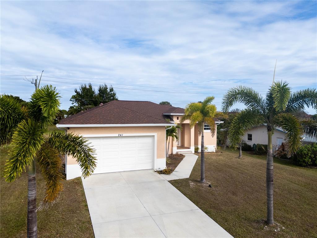 A single-story house with a white garage door, tan stucco walls, and palm trees — 241 ANNAPOLIS LANE, ROTONDA WEST, FL