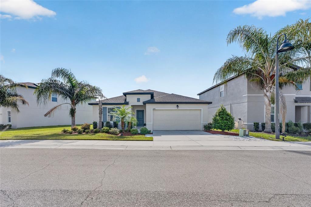 A single-story suburban house with a two-car garage and palm trees in the front yard — 6938 SHELBY LYNN WAY, ZEPHYRHILLS, FL