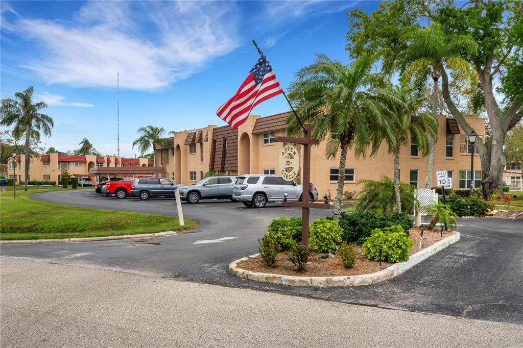 An American flag flies above the entrance sign of a multi-story apartment complex with parking — 121 ASPEN CIRCLE UNIT 121, SEMINOLE, FL