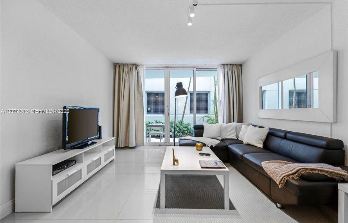 A living room features a black leather sectional, white coffee table, and sliding glass doors — 3901 S Ocean Dr # 1B, Hollywood FL 33019, HOLLYWOOD, FL