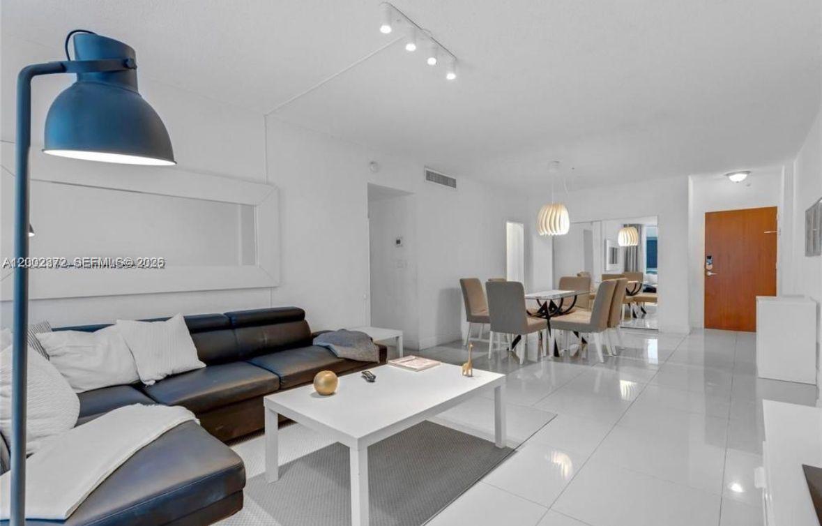 A living room with white tile floors, a black leather sofa, and a dining area — 3901 S Ocean Dr # 1B, Hollywood FL 33019, HOLLYWOOD, FL