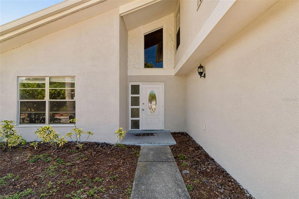 A concrete walkway leads to the white front door of a stucco house — 4163 MALLARD DRIVE, SAFETY HARBOR, FL
